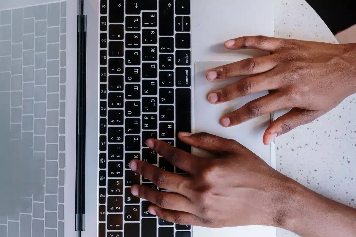 Mani che digitano su una tastiera con schermo di computer in background illuminato da luce d'ufficio