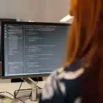 Sviluppatore al lavoro su più monitor con codice e interfacce app, ambiente di sviluppo moderno