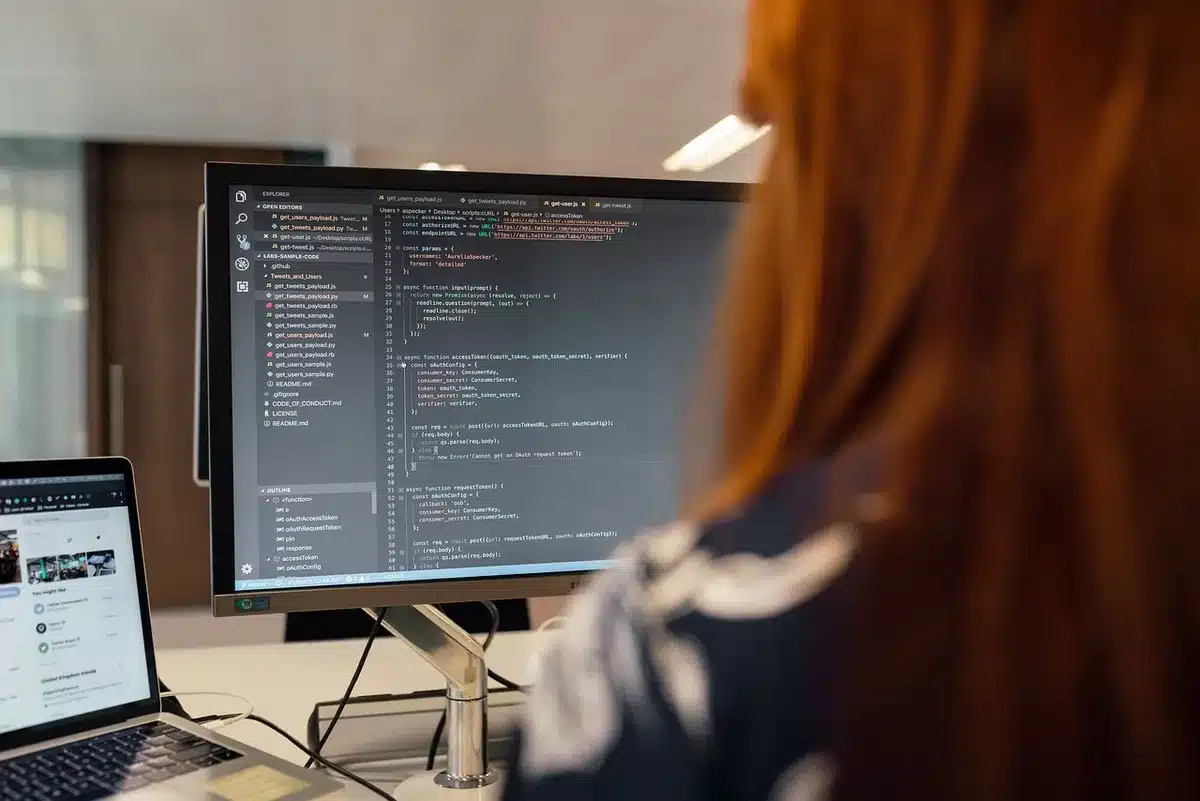 Sviluppatore al lavoro su più monitor con codice e interfacce app, ambiente di sviluppo moderno