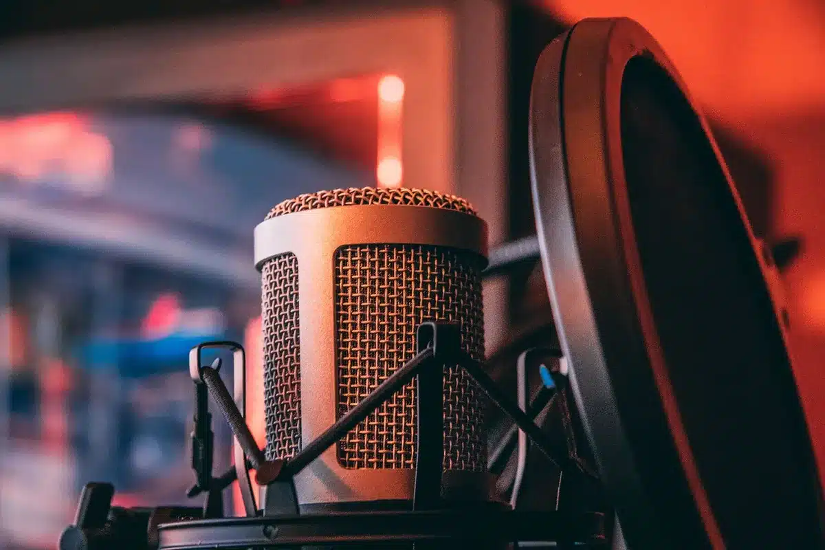 Microfono professionale in uno studio podcast con schermo di computer e cuffie sullo sfondo.