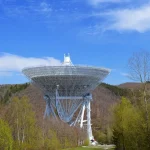 Tecnico anonimo regola uno specchio segmentato in una struttura di assemblaggio spaziale con illuminazione infrarossa.