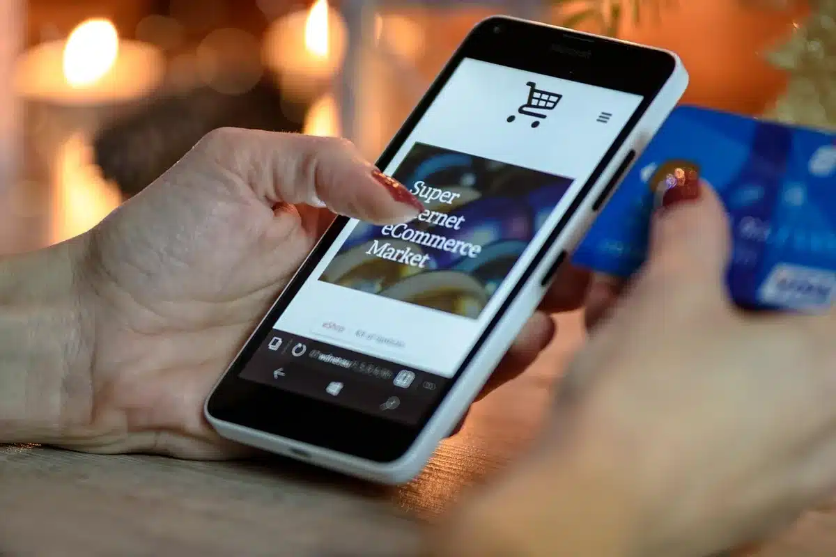 Mani di un acquirente che tengono uno smartphone con lista acquisti vicino a una bandiera americana su tavolo da cucina